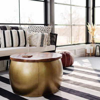 A large dark gold coffee table with wood top sits in front of a black wicker couch with cream cushions in a four season porch with modern farmhouse interior styling by Lauren and Janelle from Stone + Suede.